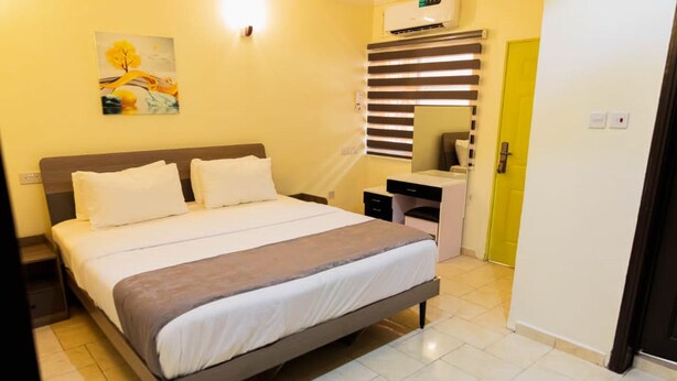 A hotel room with a bed, bedside table, and a desk with a chair. - Captivating 3-bed Apartment in Lagos (Lekki)
