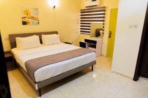A hotel room with a bed, bedside table, and a desk with a chair. - Captivating 3-bed Apartment in Lagos (Lekki)