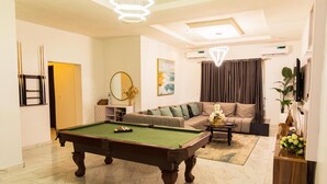 Un salon comprenant une table de billard, un canapé, une table basse et un téléviseur.