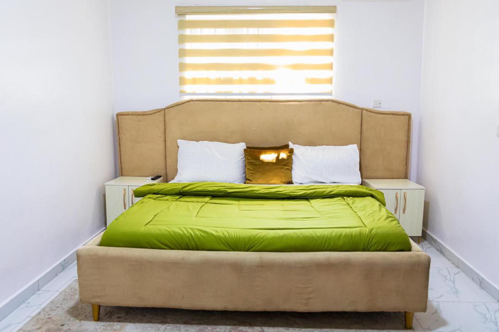 Een bed met een beige hoofdbord, groene beddengoed en twee witte kussens.