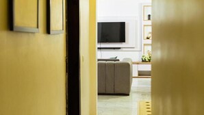 Un couloir avec un mur jaune, une porte et un téléviseur à l’arrière-plan.