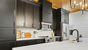 Una cocina moderna con armarios oscuros, una encimera blanca, una estufa, un microondas y un refrigerador.