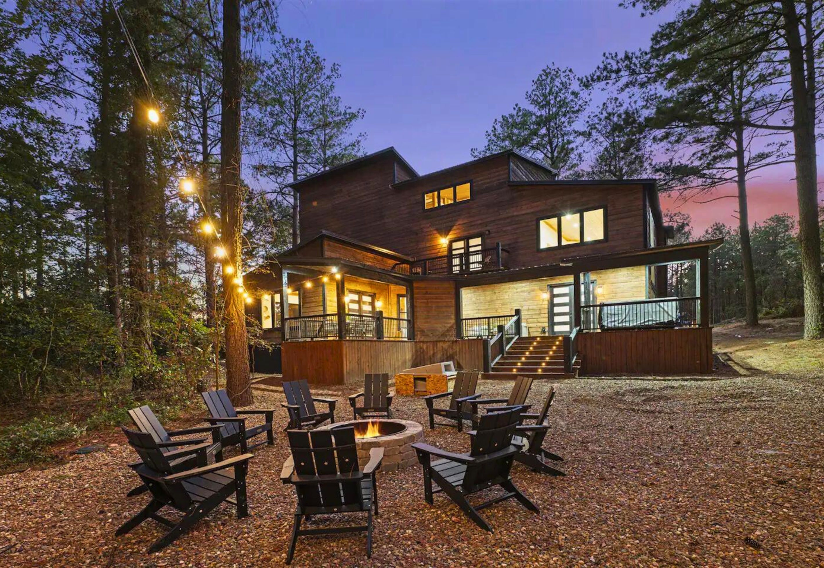 Een moderne blokhut met terras, buitenmeubilair en vuurkuil.