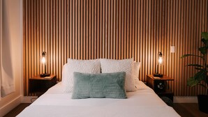 Una cama bien tendida con almohadas blancas y verdes, cabecera de listones de madera y lámparas de noche.