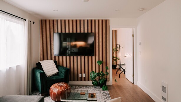 Una sala de estar moderna con televisor de pantalla plana montado en una pared de paneles de madera, un sofá verde, una mesa de centro con objetos decorativos y una planta en maceta.