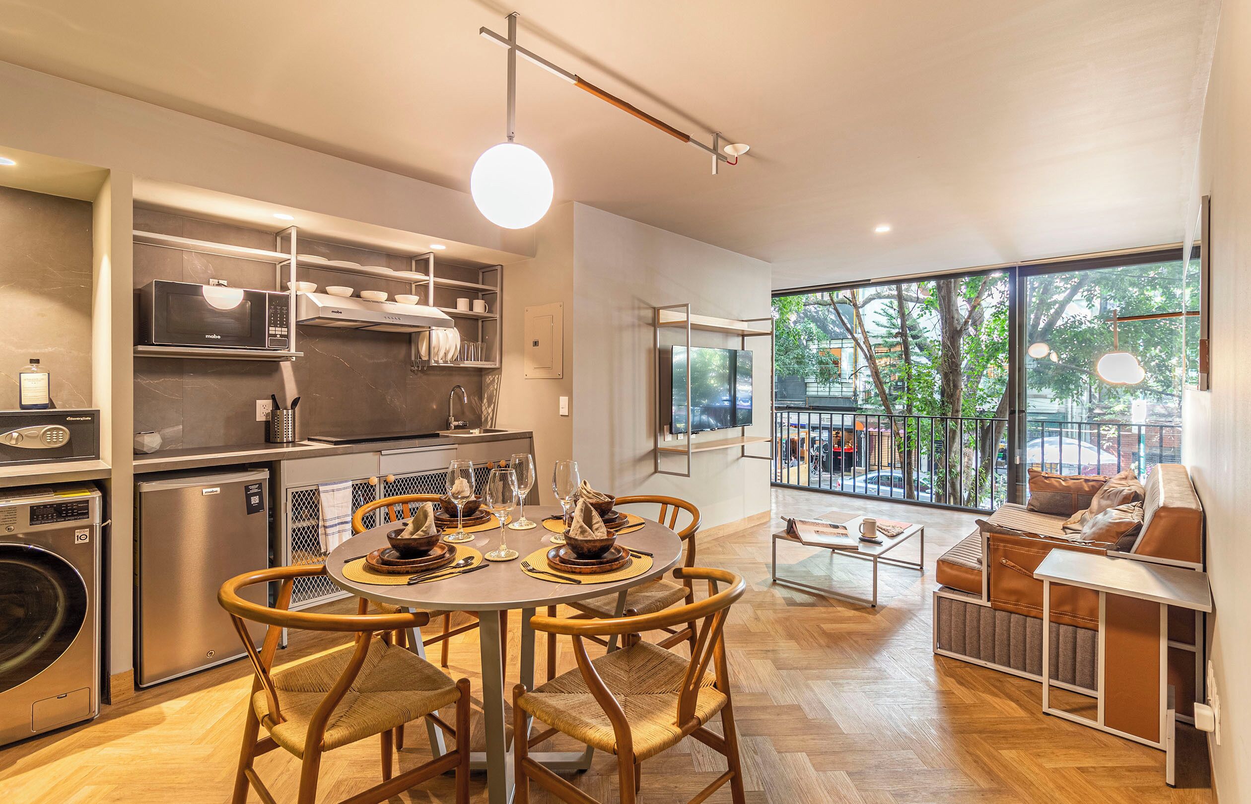 A modern kitchen with built-in appliances, a dining area with a round table and chairs, and a seating area with a sofa and a view of the outdoors.