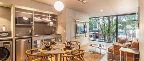 A modern kitchen with built-in appliances, a dining area with a round table and chairs, and a seating area with a sofa and a view of the outdoors.