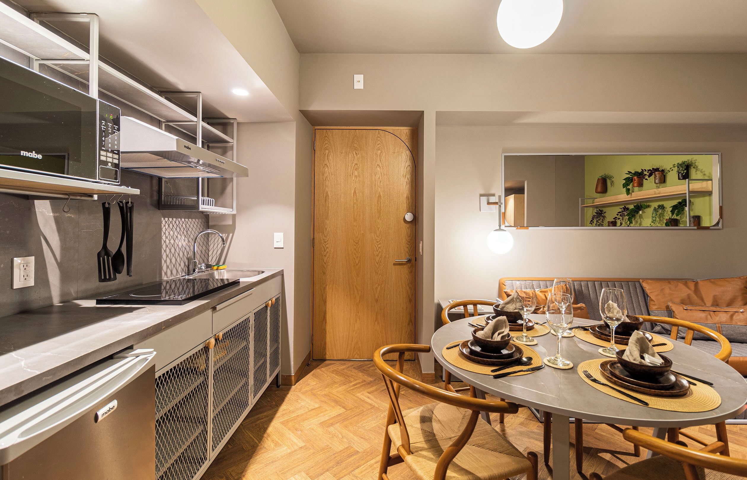 Uma cozinha moderna com fogão embutido, uma porta de madeira e um espaço de jantar com mesa redonda posta para quatro pessoas.