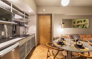 Une cuisine moderne dotée d’une cuisinière intégrée, d’une porte en bois et d’un coin repas avec une table ronde prévue pour quatre personnes.