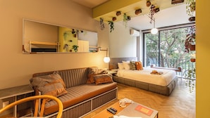 Une chambre d’hôtel moderne équipée d’un canapé, d’un lit, d’un bureau et d’une grande fenêtre donnant sur un paysage arboré.