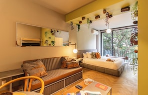 Une chambre d’hôtel moderne équipée d’un canapé, d’un lit, d’un bureau et d’une grande fenêtre donnant sur un paysage arboré.