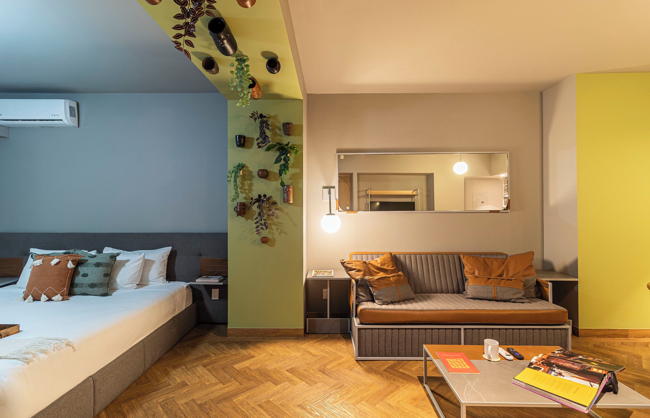 Un dormitorio moderno con cama, sofá, mesita de noche, espejo y un arreglo de plantas en la pared.