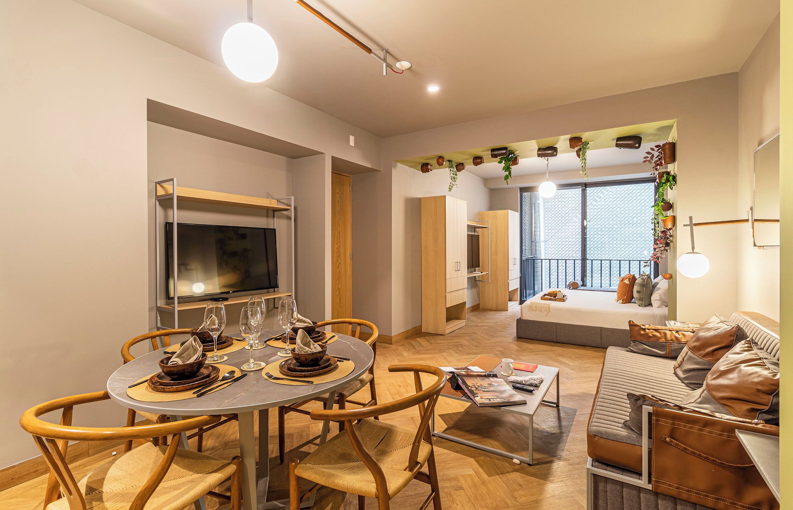 A modern living space with a dining area, kitchen, and a balcony with plants.
