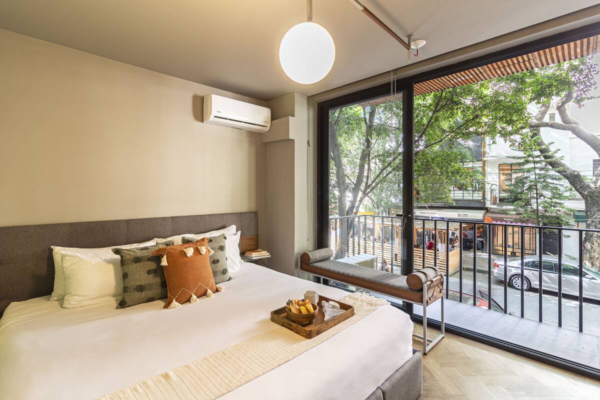 Una habitación de hotel moderna con una cama grande, vista a la calle y un balcón con banco.