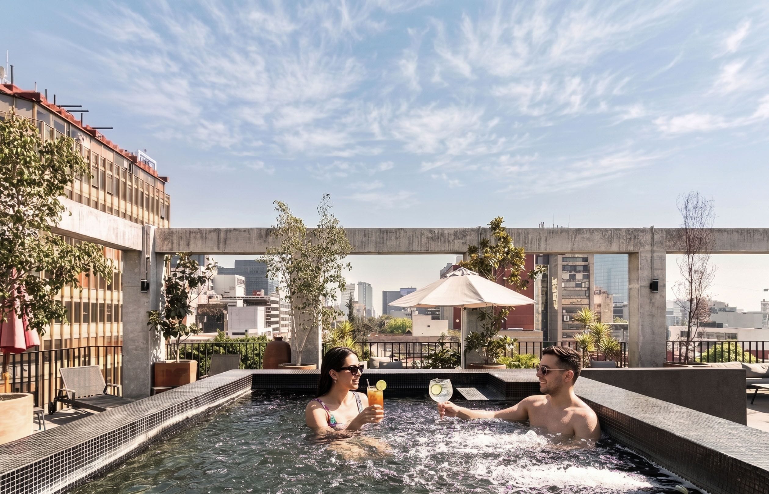 A rooftop pool area with a cityscape view, including a concrete structure and potted plants.