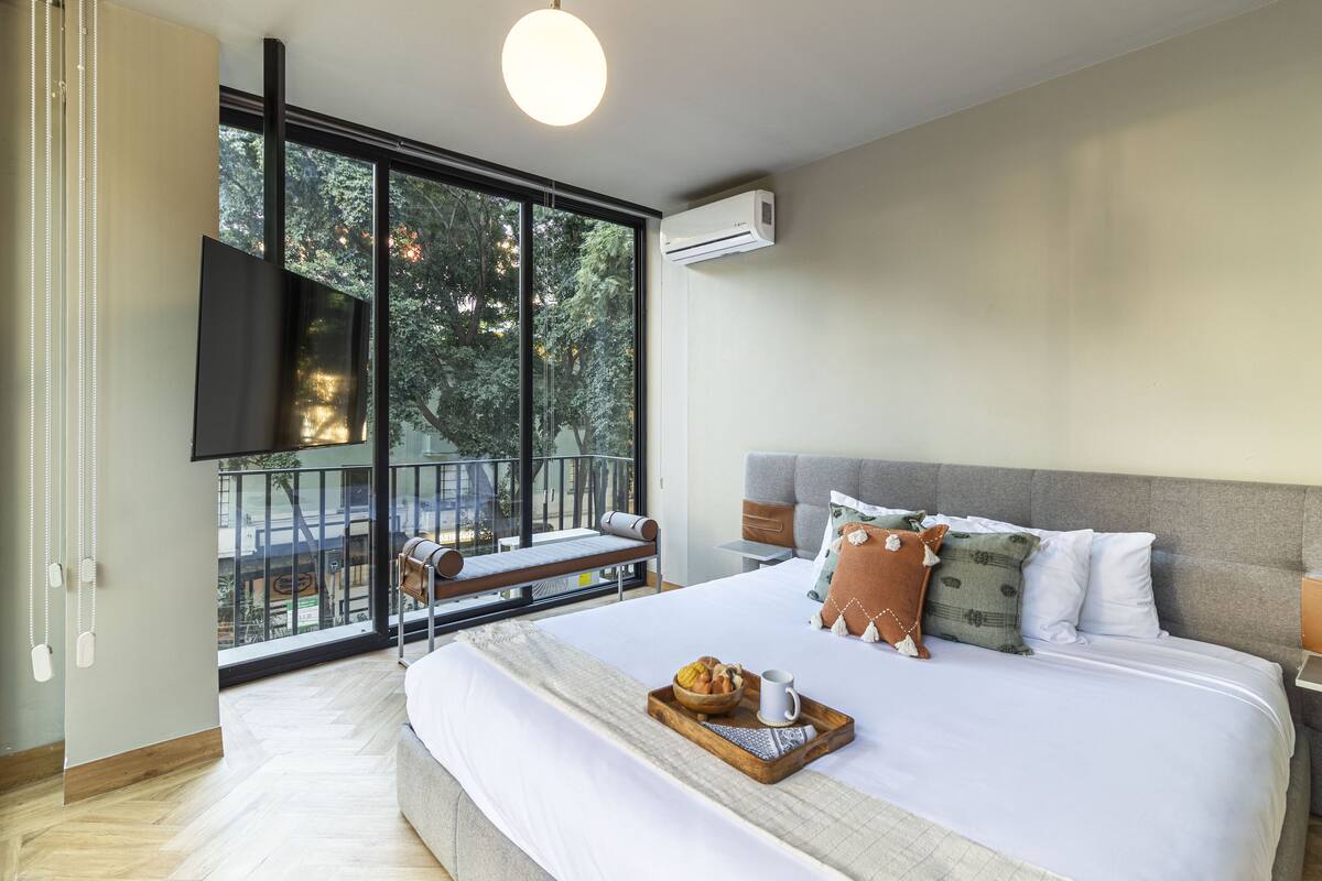 Una habitación de hotel moderna con una cama grande, un balcón con vistas, un televisor de pantalla plana y un aire acondicionado.