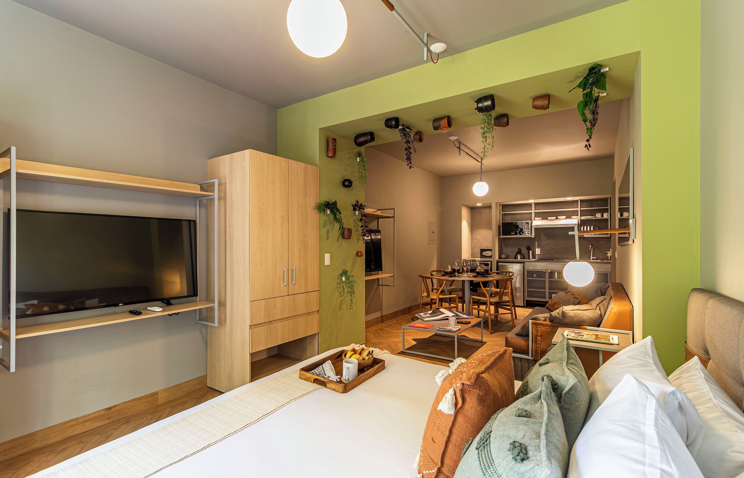 Ett kompakt bostadsutrymme med en platt-TV, träskåp, en matplats och ett litet kök.