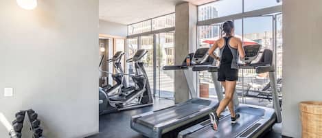 Un gimnasio con cintas de correr, mancuernas y un amplio ventanal con vista a la ciudad.