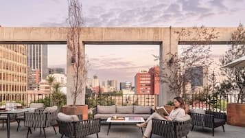 Um terraço no telhado com área de estar externa, vista da cidade e uma estrutura de concreto acima.