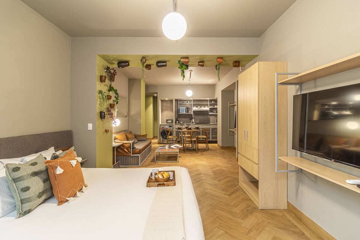 Una habitación de hotel moderna con cama, televisor, kitchenette y zona de comedor.