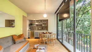 A modern apartment with a dining area, kitchen, and a large window overlooking greenery.
