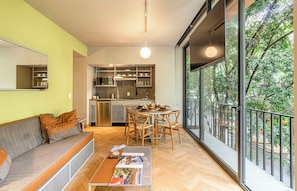A modern apartment with a dining area, kitchen, and a large window overlooking greenery.