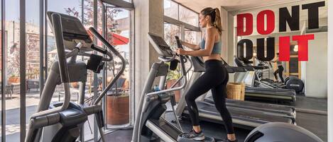 A gym with treadmills, a motivational poster, and large windows.