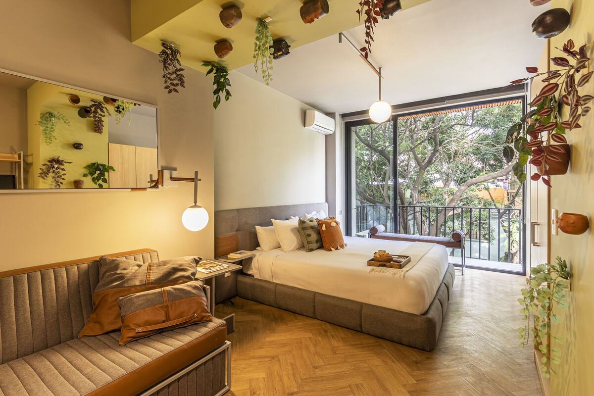 Un dormitorio moderno con una cama grande, un sofá y un balcón con plantas.