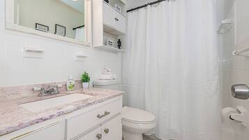 A bathroom with a marble sink, a toilet, a shower curtain, and a mirror.