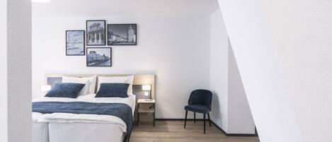 Un dormitorio moderno con una cama, mesitas de noche, una silla y cuadros en la pared.