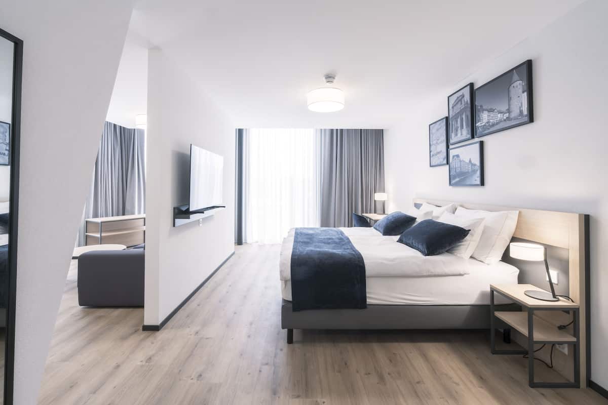 A modern hotel room with a large bed, bedside tables, a TV, and framed pictures on the wall.