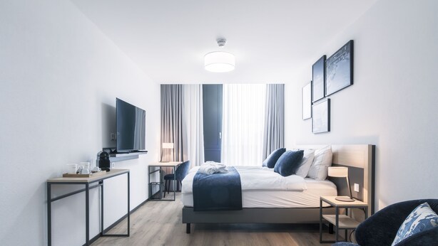 Une chambre d’hôtel moderne équipée d’un lit, d’une table de chevet, d’une chaise, d’un bureau et d’un téléviseur à écran plat.