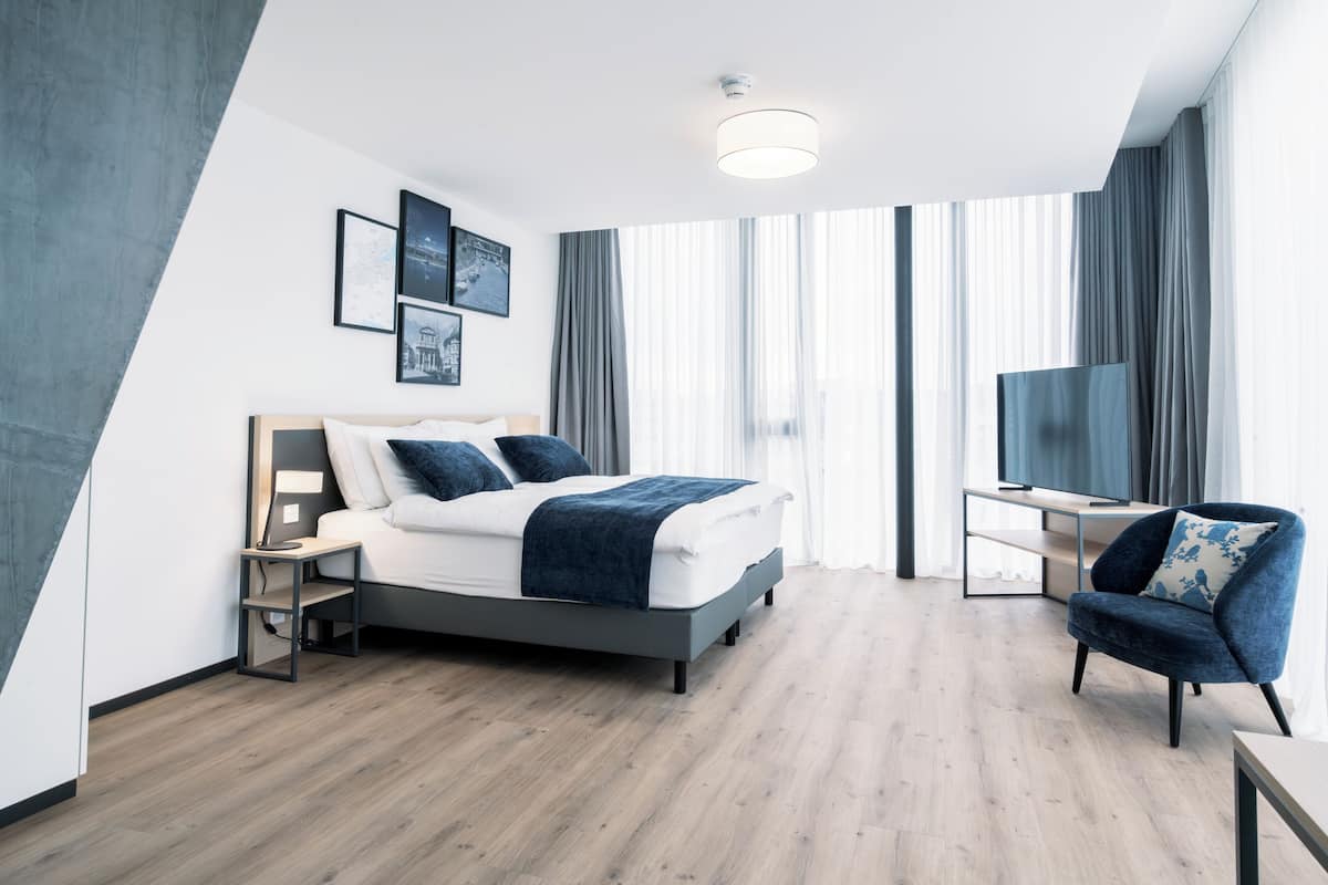 A modern hotel room with a bed, a desk, a chair, and a TV.