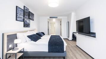 Une chambre d’hôtel moderne avec un grand lit, une table de chevet avec une lampe, un téléviseur à écran plat fixé au mur et des tableaux encadrés accrochés au mur.