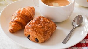 Une table dressée pour le petit-déjeuner avec des croissants, une tasse de café et un verre de jus d’orange.