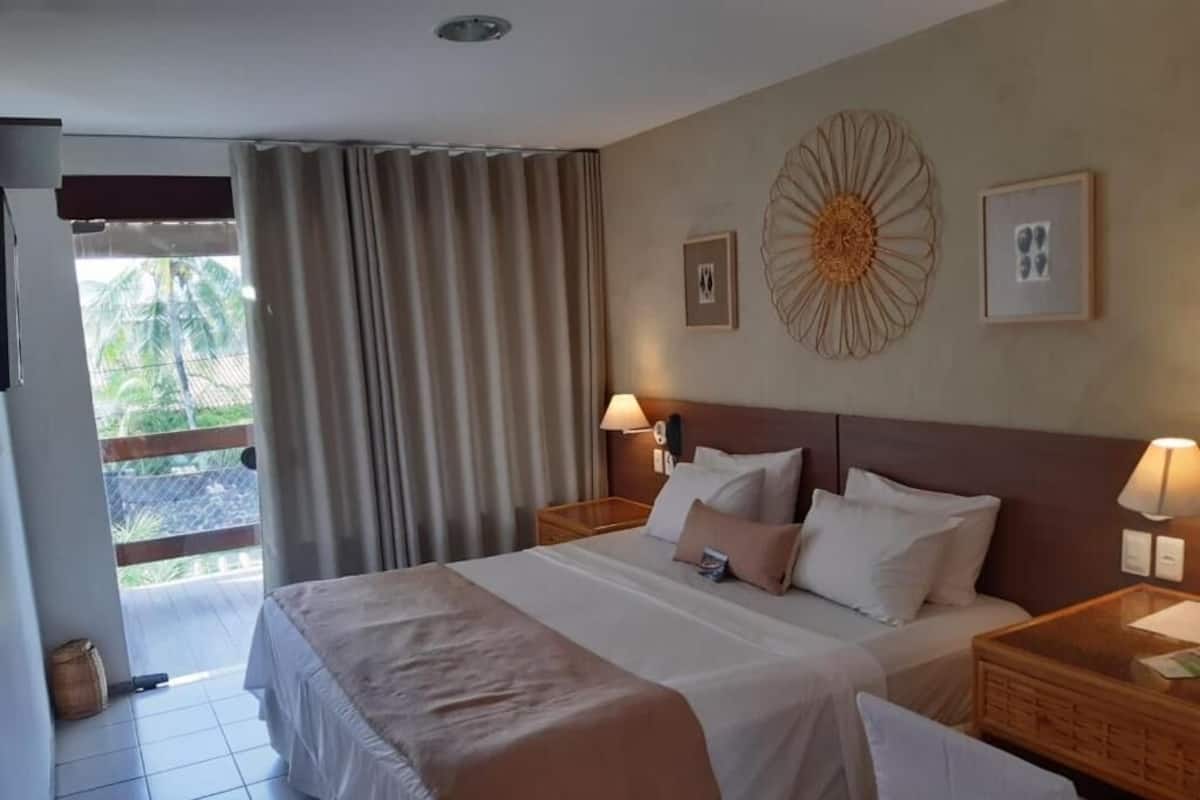 Habitación de hotel con una cama grande, dos mesitas de noche con lámparas, vista al exterior a través de una puerta corrediza y un adorno en la pared.