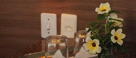Un bagno con un portalampada a parete, un vaso di vetro con fiori e un vassoio con una candela e del sale.