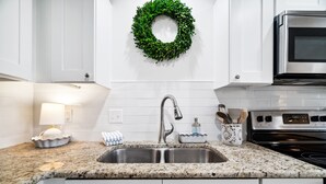 A kitchen with white cabinets, a granite countertop, a stainless steel sink, a microwave, and a green wreath on the wall. - Beachwood Villas by Panhandle Getaways (Santa Rosa Beach)