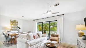 A modern living room with a white sofa, a dining table, and a large window with curtains. - Beachwood Villas by Panhandle Getaways (Santa Rosa Beach)