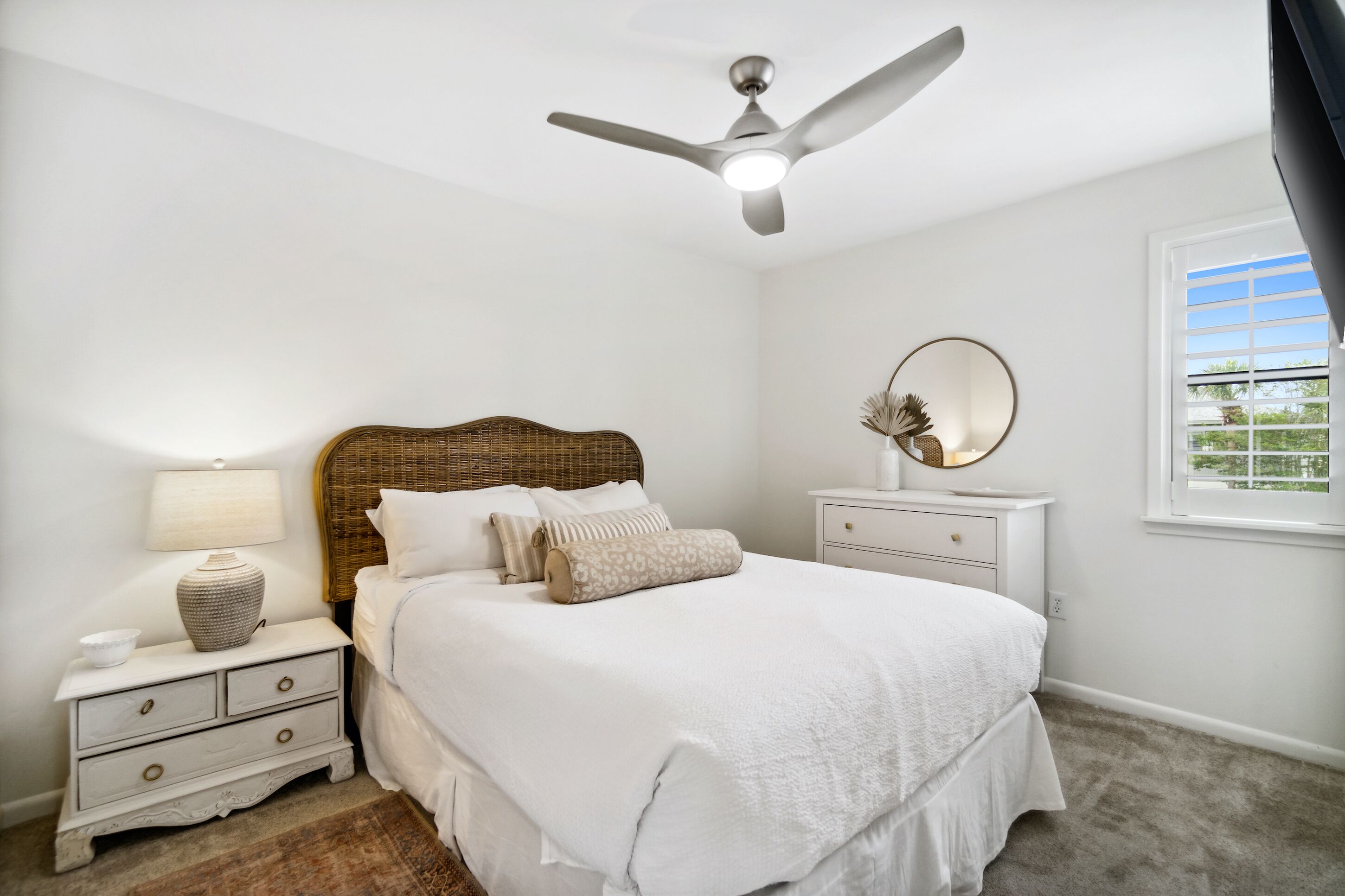 Ein Schlafzimmer mit Bett, Nachttisch, Lampe, Spiegel und Deckenventilator.