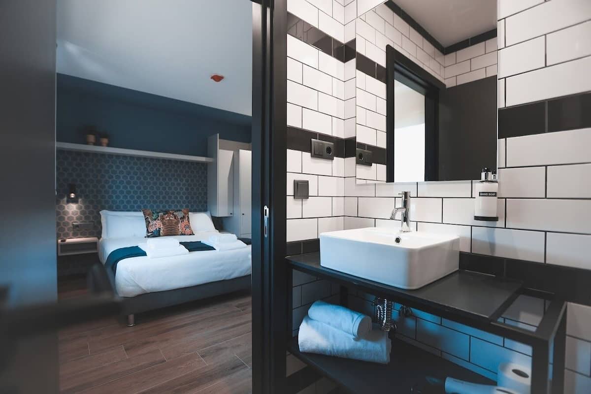 A modern hotel room with a large bed, a white sink, and a mirror above it.