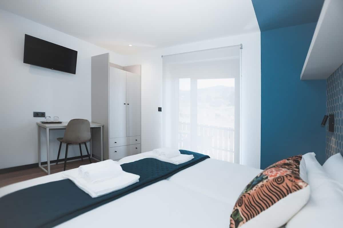 A hotel room with a bed, a desk, a chair, a TV, and a view of the outdoors.