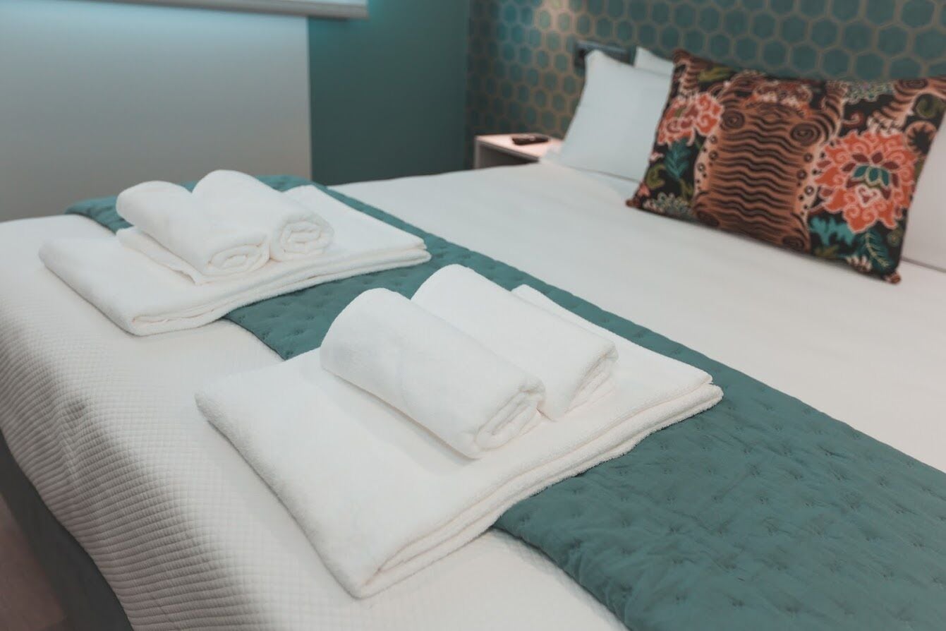 A neatly made bed with folded white towels and a teal bedspread.
