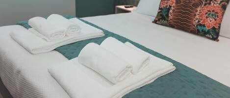 A neatly made bed with folded white towels and a teal bedspread.