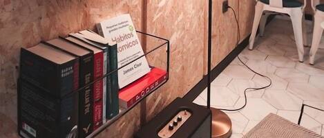 A modern room with a wooden wall, a black shelf with books, a floor lamp, and a white chair.