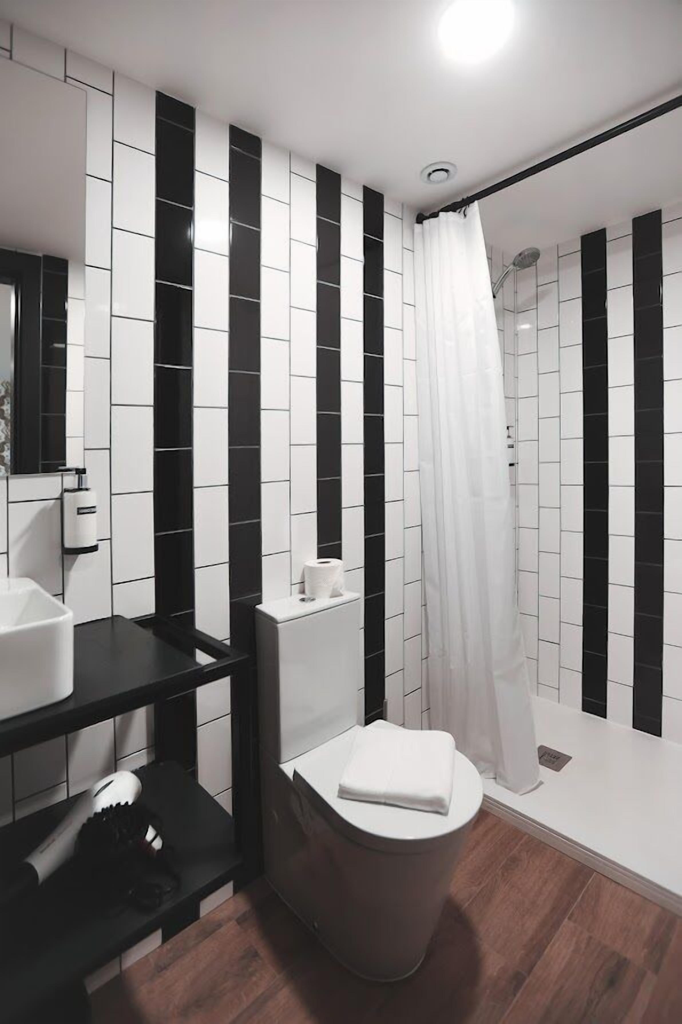 A modern bathroom with black and white tiled walls, a black countertop, a white toilet, and a shower with a white curtain.