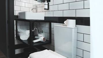 Ein modernes Badezimmer mit Toilette, einer Wand mit Schwarz-Weiß-Fliesen und einem Regal mit Handtüchern und einem Föhn.