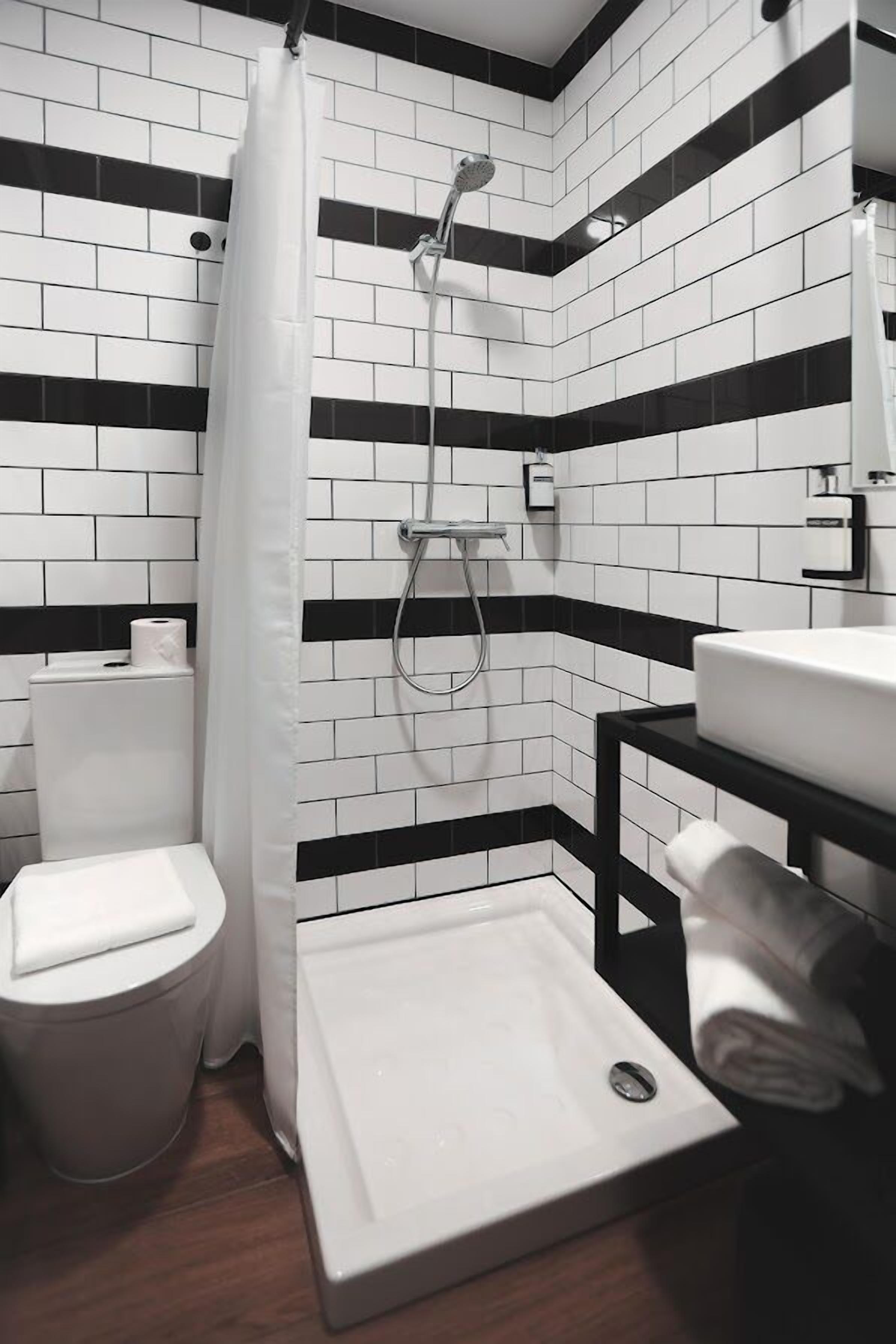A modern bathroom with a black and white tiled wall, a shower, a toilet, and a sink.