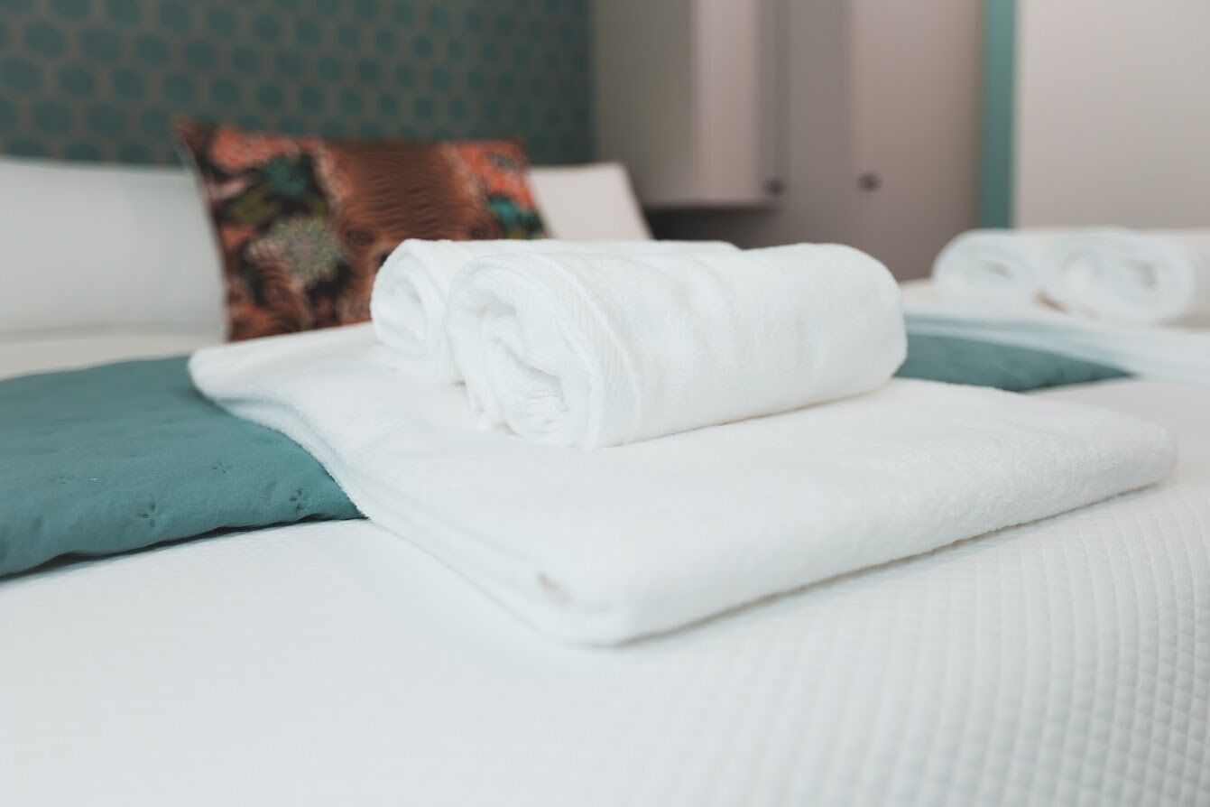 Una cama bien hecha con sábanas blancas y un cojín azul aguamarina.