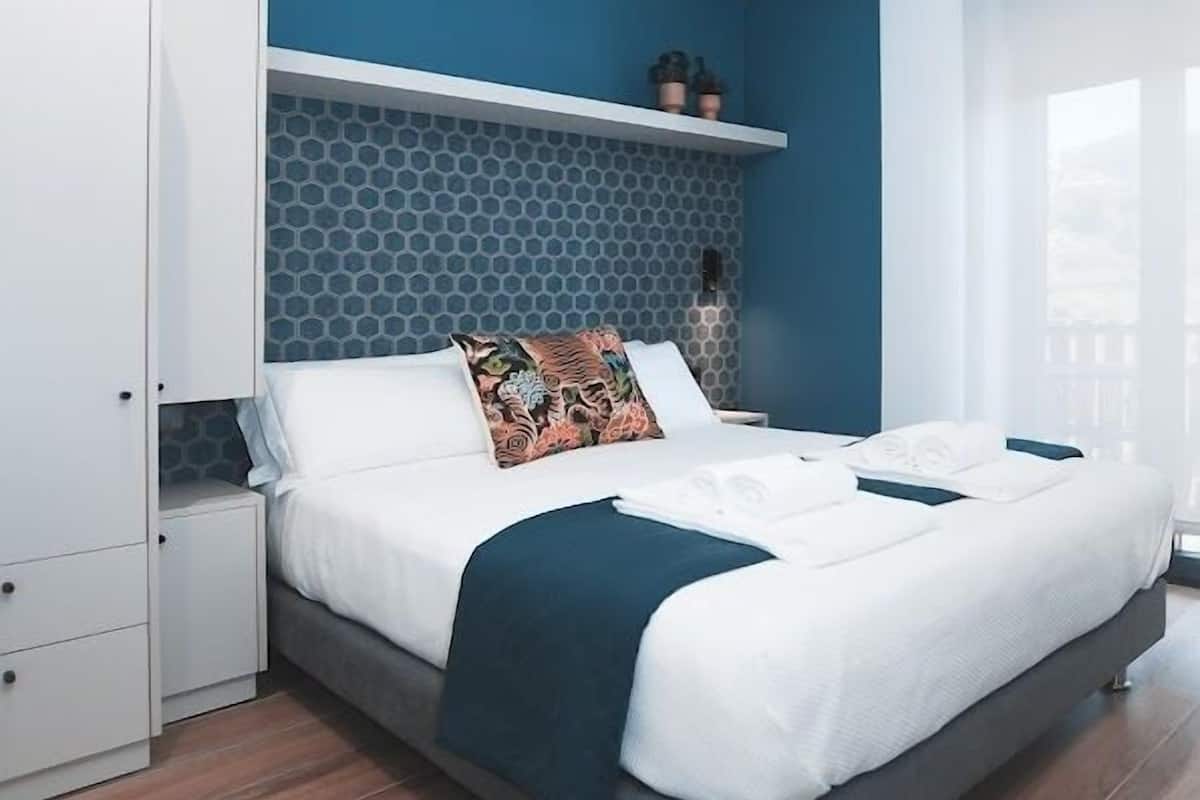 A modern bedroom with a bed, a wardrobe, and a blue accent wall.